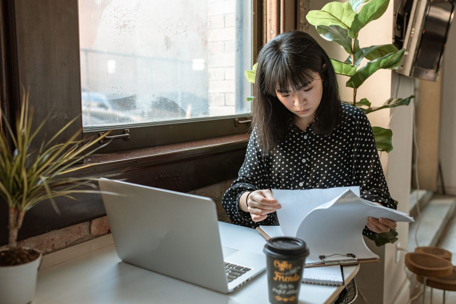Asian businesswoman reviewing documents in a modern office setting with natural light.